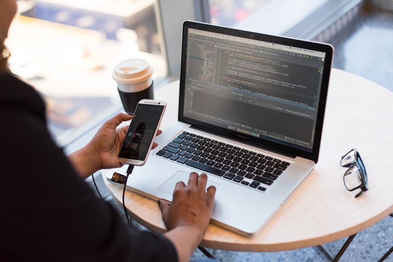 A technology professional reviewing information on a laptop and mobile phone